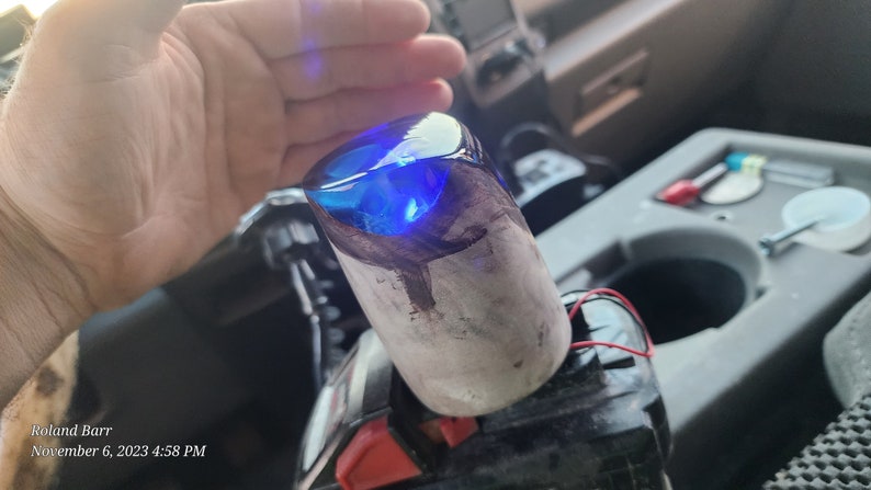 May include: A close-up of a blue resin gear shift knob with a wood base. The knob is illuminated with a bright blue light.