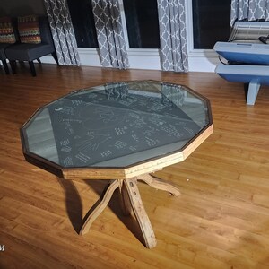 May include: A wooden octagonal table with a glass top. The table has a unique, rustic design with a starburst pattern on the top. The table is sitting on a hardwood floor.