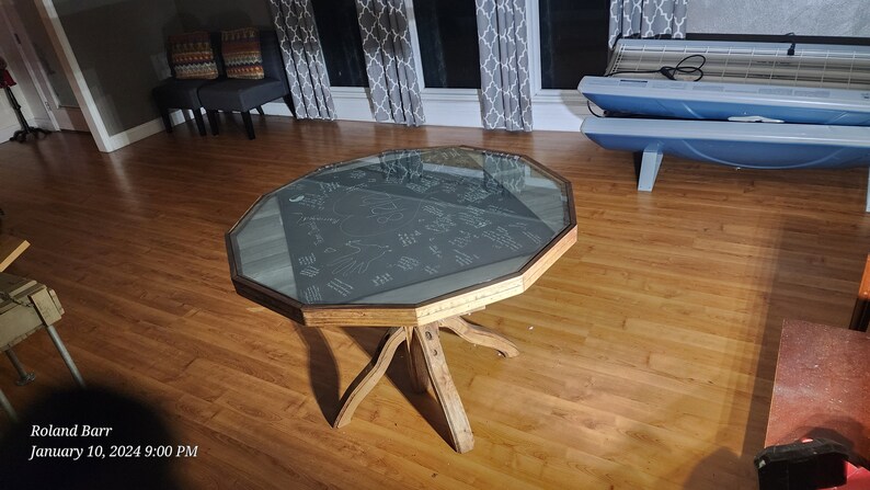 May include: A wooden octagonal table with a glass top. The table has a unique, rustic design with a starburst pattern on the top. The table is sitting on a hardwood floor.