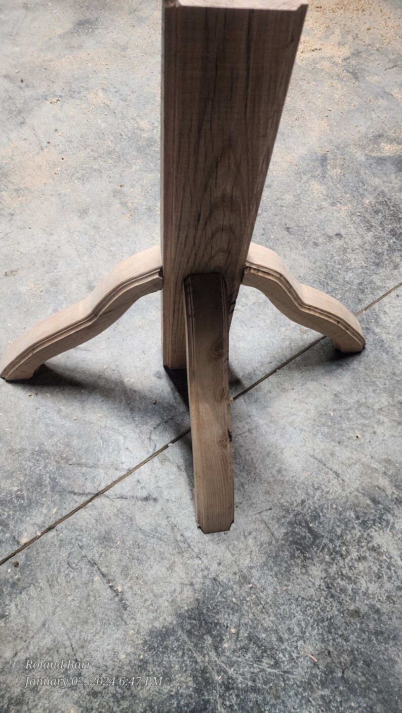 May include: A wooden table leg with a three-pronged base. The base is made of three pieces of wood that are joined together at the top. The wood is a light brown colour and has a natural finish.