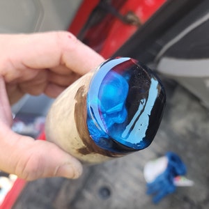 May include: Close-up of a wooden handle with a blue and black resin cap. The resin has a swirling pattern and a glossy finish.