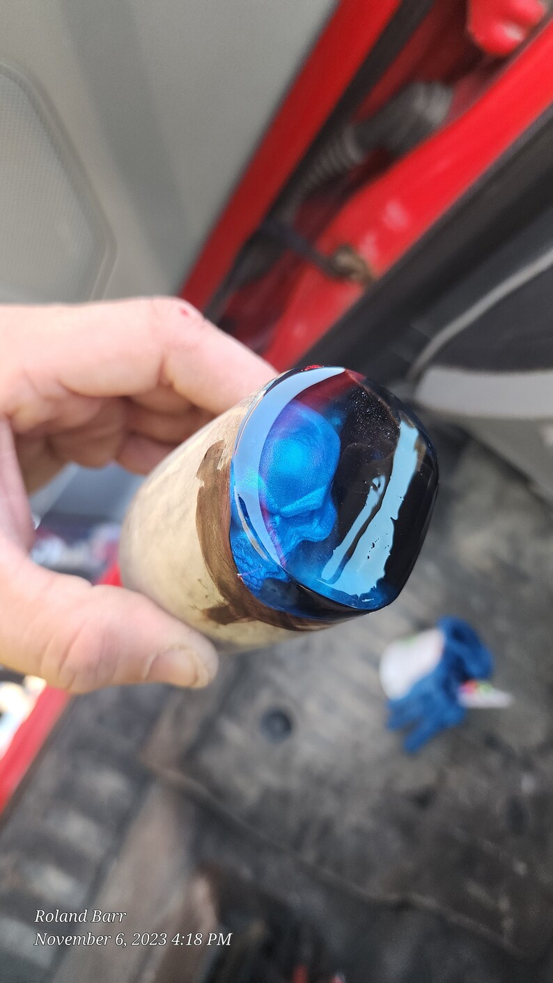 May include: Close-up of a wooden handle with a blue and black resin cap. The resin has a swirling pattern and a glossy finish.