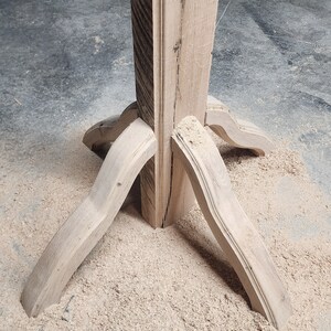 May include: A wooden table base with four legs that are curved and joined at the top. The base is made of unfinished wood and is sitting on a pile of sawdust.