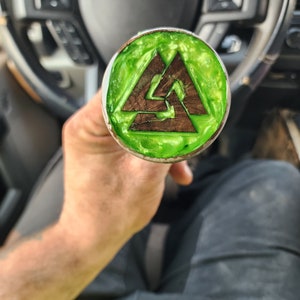 May include: A green and brown wooden knob with a triangular design. The knob is held in a person's hand.