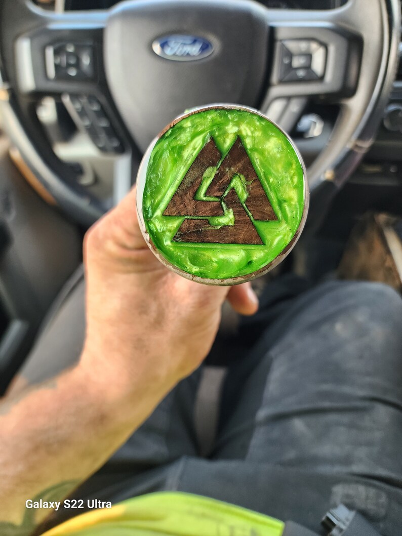 May include: A green and brown wooden knob with a triangular design. The knob is held in a person's hand.