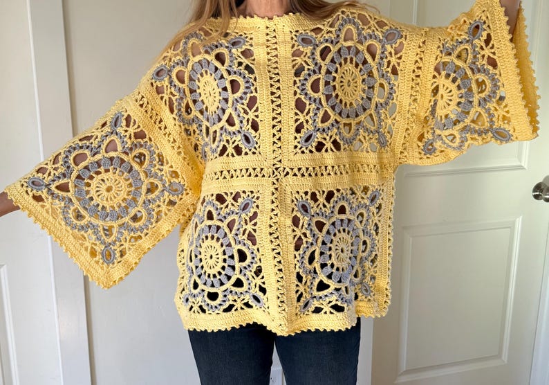 May include: A yellow crochet top with a square pattern design. The top features a floral design in gray and yellow. The sleeves are wide and flared. The top is made of a soft, open-weave material.