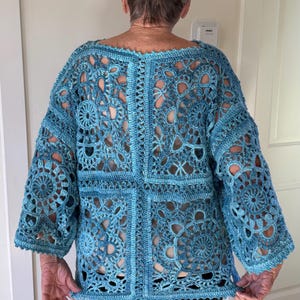 May include: A light blue crochet top with a unique openwork design. The top features a round neckline and three-quarter sleeves. The intricate pattern creates a delicate, airy look. The garment is worn with black pants.