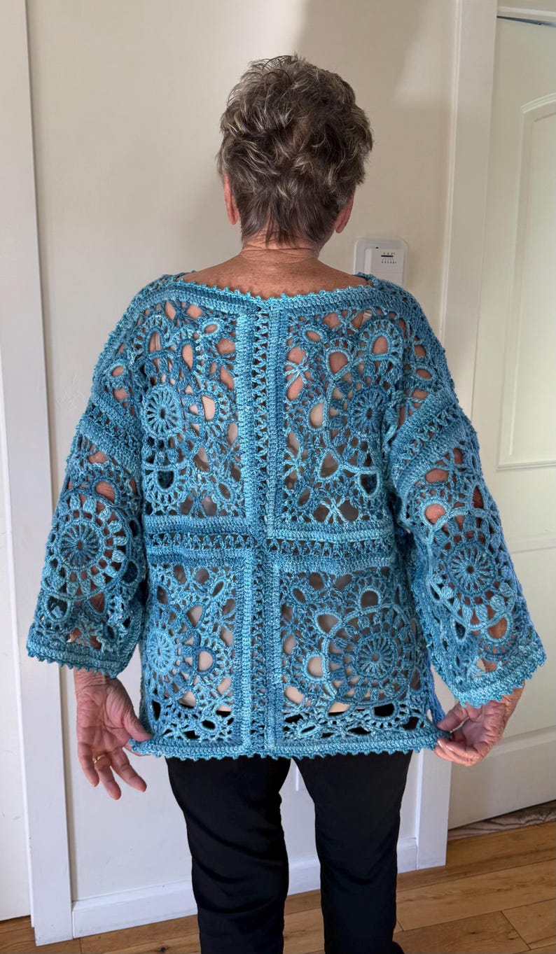 May include: A light blue crochet top with a unique openwork design. The top features a round neckline and three-quarter sleeves. The intricate pattern creates a delicate, airy look. The garment is worn with black pants.
