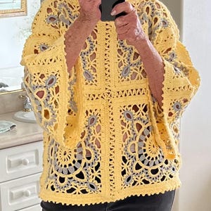 May include: A yellow crochet top with a floral design and gray accents. The top has wide sleeves and a detailed openwork pattern. The crochet work is visible, showcasing the texture and craftsmanship of the garment.