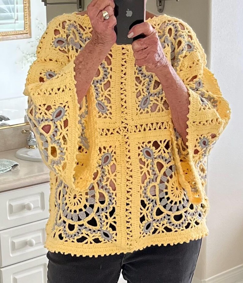May include: A yellow crochet top with a floral design and gray accents. The top has wide sleeves and a detailed openwork pattern. The crochet work is visible, showcasing the texture and craftsmanship of the garment.