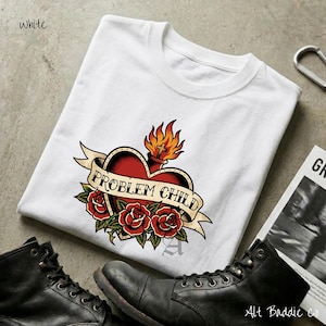 May include: White t-shirt featuring a heart-shaped tattoo design with the words "PROBLEM CHILD" on a banner. The design includes red roses, flames, and a traditional tattoo style. Black boots are visible in the foreground.