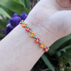 May include: A beaded bracelet with a repeating pattern of small orange, yellow, and green flowers.