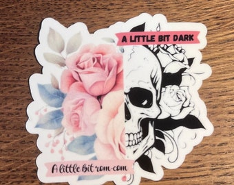 May include: A sticker featuring a black and white skull on the right side and pink roses on the left. The sticker includes the text "A little bit dark" and "A little bit rom-com".