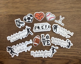 Op de afbeelding: Een set van 11 stickers met sportthema's. De stickers zijn wit met zwarte tekst en afbeeldingen. De tekst omvat "Mijn boekvriend is een honkballer", "Mijn boekvriend is een voetballer", "Mijn boekvriend is een hockeyer", "Mijn boekvriend is een basketballer", "Mijn boekvriend is een voetballer", en "Ik hou van sport... Sportromanze". De stickers bevatten ook afbeeldingen van een honkbal, een basketbal, een voetbal, een voetbal, hockeysticks en schaatsen.