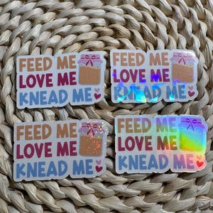 May include: Four rectangular stickers featuring the text FEED ME LOVE ME KNEAD ME in brown, pink, and blue. Each sticker includes an illustration of a glass jar with a bow on the lid and small hearts. Some stickers have a holographic finish.