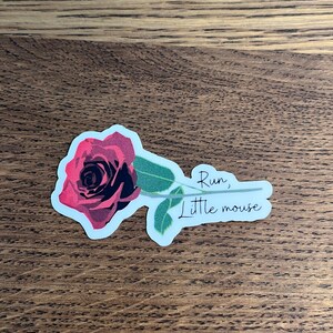 May include: A sticker with a red rose and the text "Run, little mouse" in black cursive.