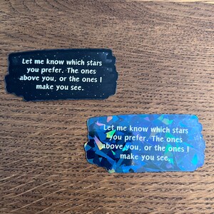 May include: Two black and white stickers with a glittery iridescent finish. The stickers feature the text "Let me know which stars you prefer. The ones above you, or the ones I make you see."