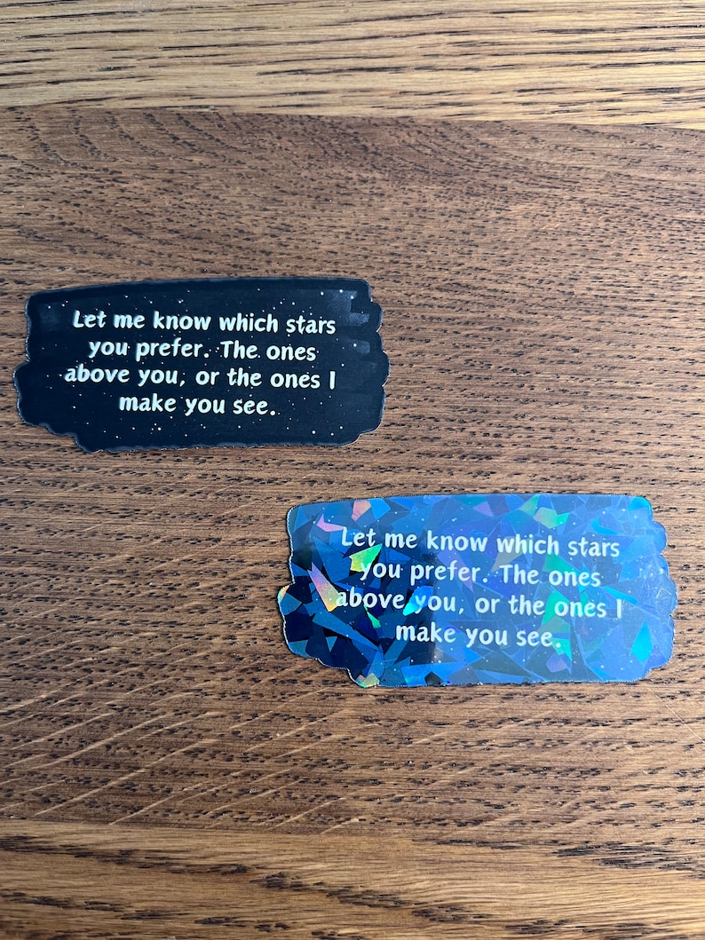 May include: Two black and white stickers with a glittery iridescent finish. The stickers feature the text "Let me know which stars you prefer. The ones above you, or the ones I make you see."