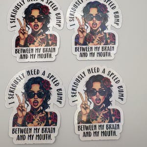 以下が含まれることがあります： サングラス、タトゥー、ピースサインをした女性が描かれた4つのステッカー。ステッカーのテキストは「私は真剣に私の脳と私の口の間にスピードバンプが必要です」と書かれています。