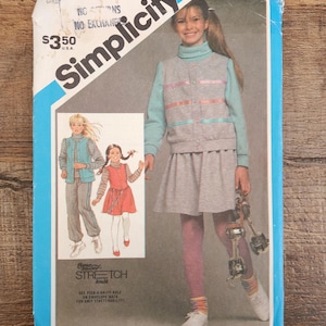 May include: A Simplicity sewing pattern envelope for a grey and light blue outfit featuring a turtleneck top, a button-down vest with horizontal ribbons, and a skirt. The cover displays illustrations of the finished garments and the text Time Saver Stretch Knit.