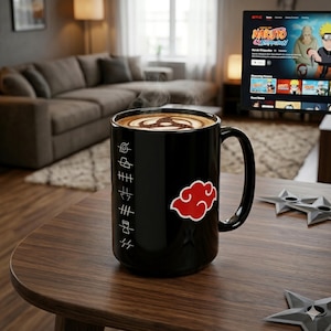 Pode incluir: Uma caneca de cerâmica preta com um design de nuvem vermelha e caracteres japoneses. A caneca contém uma bebida de café com um design decorativo. A caneca está em uma mesa de madeira com estrelas ninja.