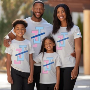 Peut inclure: Une famille de quatre personnes portant des t-shirts blancs assortis. Chaque chemise pr&eacute;sente un motif rose, bleu clair et une ligne diagonale bleue. La famille sourit et pose pour une photo.