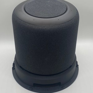 May include: A black cylindrical smart speaker with a fabric covering and a black base. The speaker has a circular top with a fabric covering.