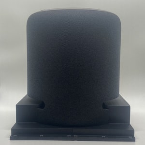 May include: A black cylindrical smart speaker with a fabric covering sits on a black stand with a cutout for the power cord.