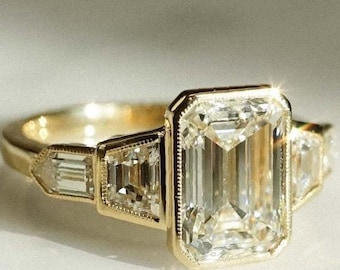 Pode incluir: Um anel de noivado de ouro com um grande diamante de corte esmeralda e dois diamantes baguette menores na banda.