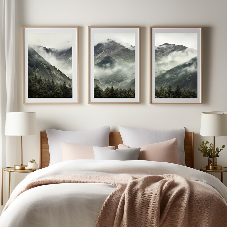 May include: Three framed landscape photographs of a mountain range with fog and trees. The photographs are hung on a white wall above a bed with white bedding and a pink throw blanket.