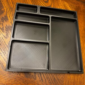 K&ouml;nnte beinhalten: Ein schwarzes Plastik-Organizer-Tablett mit sechs F&auml;chern in verschiedenen Gr&ouml;&szlig;en. Das Tablett ist f&uuml;r die Aufbewahrung von kleinen Gegenst&auml;nden konzipiert und eignet sich ideal zum Organisieren eines Schreibtisches oder Arbeitsplatzes.