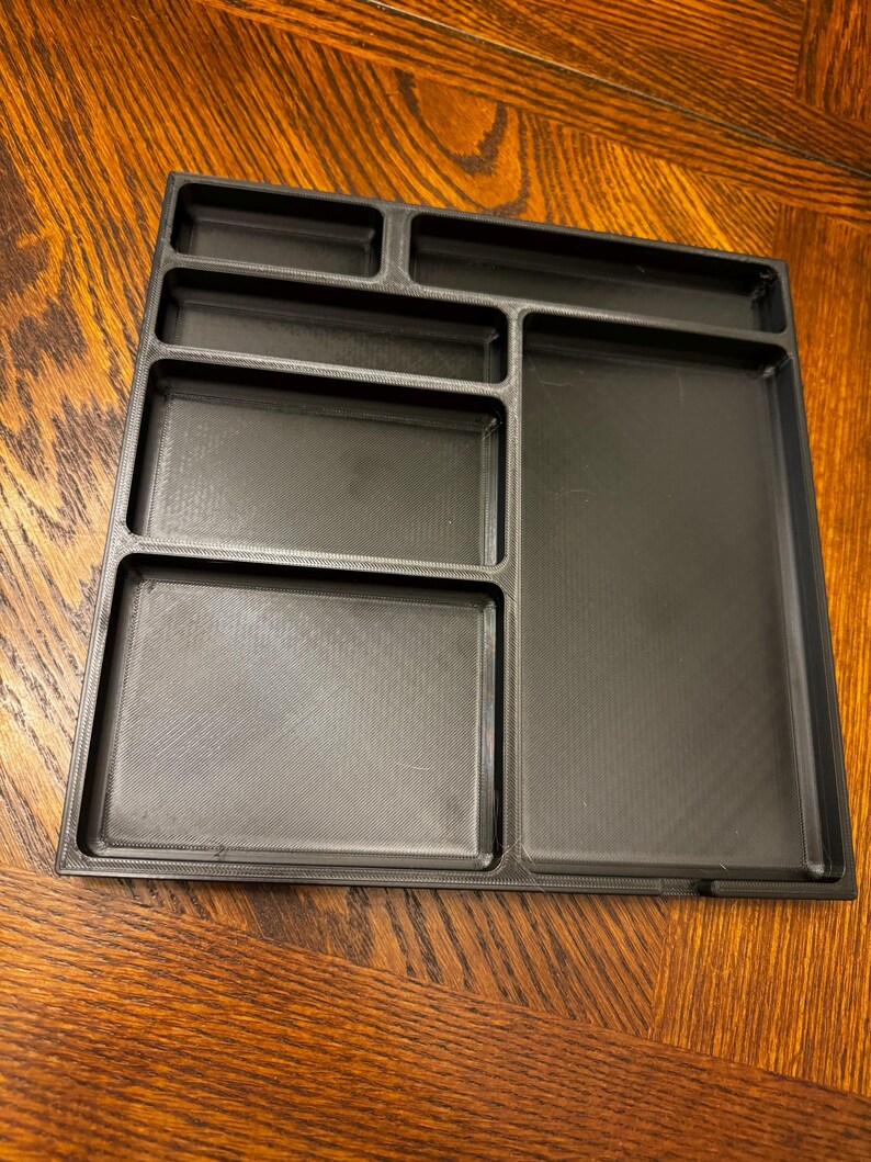 K&ouml;nnte beinhalten: Ein schwarzes Plastik-Organizer-Tablett mit sechs F&auml;chern in verschiedenen Gr&ouml;&szlig;en. Das Tablett ist f&uuml;r die Aufbewahrung von kleinen Gegenst&auml;nden konzipiert und eignet sich ideal zum Organisieren eines Schreibtisches oder Arbeitsplatzes.