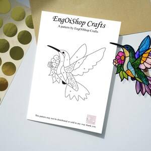 May include: A craft project featuring a hummingbird design. The image includes a black and white line drawing of a hummingbird with numbered sections, a colorful hummingbird decoration, and gold foil stickers. The text reads "EngOiShop Crafts".
