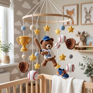 May include: A handmade crochet baby mobile featuring a baseball theme. The mobile includes a teddy bear holding a bat, baseballs, stars, a trophy, a baseball glove, and a blue shoe. The mobile hangs from a wooden ring and is suspended over a crib.