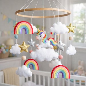 May include: A whimsical baby mobile featuring a unicorn, rainbows, clouds, and stars. The mobile has a wooden ring and is suspended by strings. The unicorn has a colorful mane and tail. The rainbows are in various colors, and the stars are gold and silver.