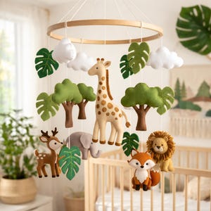 May include: A baby mobile featuring felt animal figures including a giraffe, deer, elephant, fox, and lion. The mobile also includes green felt leaves, white clouds, and green trees, all suspended from a wooden hoop.