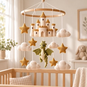 May include: A hanging mobile featuring a central crocheted castle in cream and tan, surrounded by a green crocheted dragon, several cream-colored clouds, and mustard yellow stars, all suspended from a circular wooden frame with white strings.