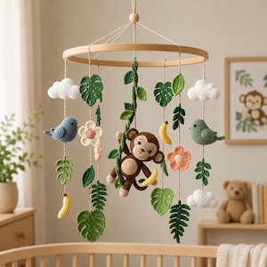 May include: A handcrafted baby mobile featuring a wooden ring with hanging crochet elements. The mobile includes a brown monkey, blue and green birds, white clouds, green leaves, flowers, and yellow bananas. The mobile is designed to hang above a crib.