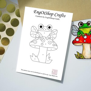 May include: A black and white line art pattern of a frog sitting on a mushroom with wings. The pattern is numbered for a paint-by-number craft project. The text "EngOiShop Crafts" and "A pattern by EngOiShop Crafts" is at the top of the page. The text "This pattern may not be distributed or sold in any way thank you." is at the bottom of the page.