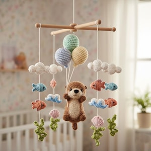 May include: A handmade baby mobile with a brown otter holding three crochet balloons. The mobile includes white clouds, colourful fish, and green seaweed. The wooden frame suspends the charming, whimsical nursery decor.