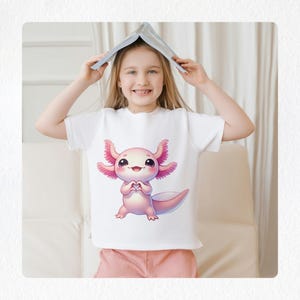May include: A white t-shirt featuring a cartoon axolotl design in pink and white. The axolotl is making a heart shape with its hands. The person is wearing pink shorts and holding a book over their head.
