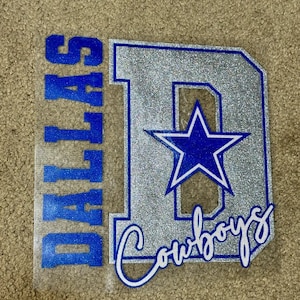 May include: A silver glitter iron-on design with a blue star and the text "Dallas Cowboys" in a white cursive font.