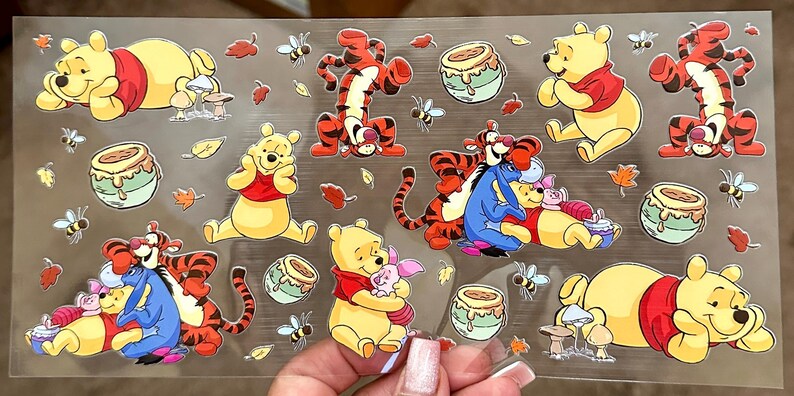 Puede incluir: Una hoja de pegatinas de vinilo transparente con los personajes de Winnie de Pooh y Tigger. Las pegatinas son amarillas, rojas y naranjas con contornos negros. Los personajes est&aacute;n en varias poses, incluyendo sentados, de pie y abraz&aacute;ndose. Tambi&eacute;n hay im&aacute;genes de tarros de miel y hojas.