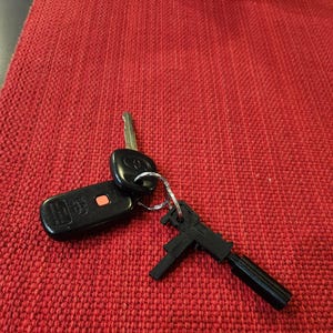 May include: A black keychain with a small toy gun attached to a set of car keys.