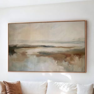 May include: A living room scene featuring a large abstract landscape painting in neutral tones above a white sofa with brown accent pillows. A wooden coffee table and a leather chair complete the decor. The text "BRUSH & PALETTES art collective" is at the bottom.
