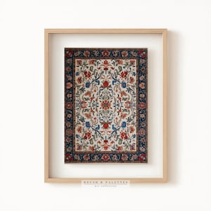 May include: Framed art print featuring a detailed floral rug design. The rug has a cream background with red, blue, and orange floral patterns. A dark blue border frames the rug. The frame is light wood. The text "BRUSH & PALETTES art collective" is at the bottom.