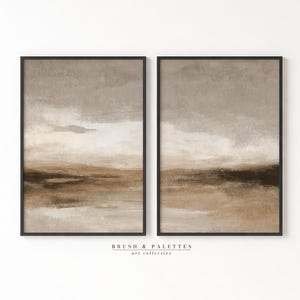 Pode incluir: Duas impressões de arte de parede retangulares verticais em molduras pretas com uma pintura de paisagem abstrata com faixas horizontais em camadas em tons de bege, taupe e castanho escuro. O texto BRUSH & PALETTES art collective aparece abaixo.