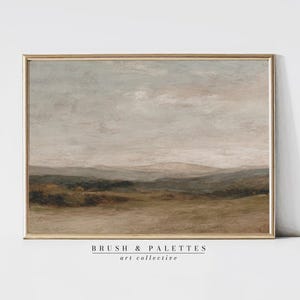 May include: A framed landscape painting with a gold-colored frame. The artwork depicts a muted color palette of beige, brown, and gray, with a cloudy sky and rolling hills. The text "BRUSH & PALETTES art collective" is at the bottom.