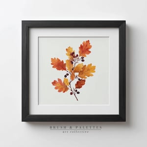 May include: A framed art print featuring a watercolor illustration of autumn leaves and berries. The leaves are in shades of orange and yellow, with small dark berries. The artwork is set against a white background and framed in a black frame. The text "BRUSH & PALETTES art collective" is at the bottom.