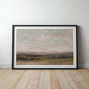 May include: A framed landscape painting with a black frame. The artwork depicts a serene scene of rolling hills and a cloudy sky, with muted tones of green, brown, and gray. The painting is displayed on a light wood floor.